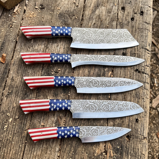 Five fixed-blade knives with patterned steel blades and red, white, and blue American flag-patterned handles, arranged diagonally on a rustic wooden surface.