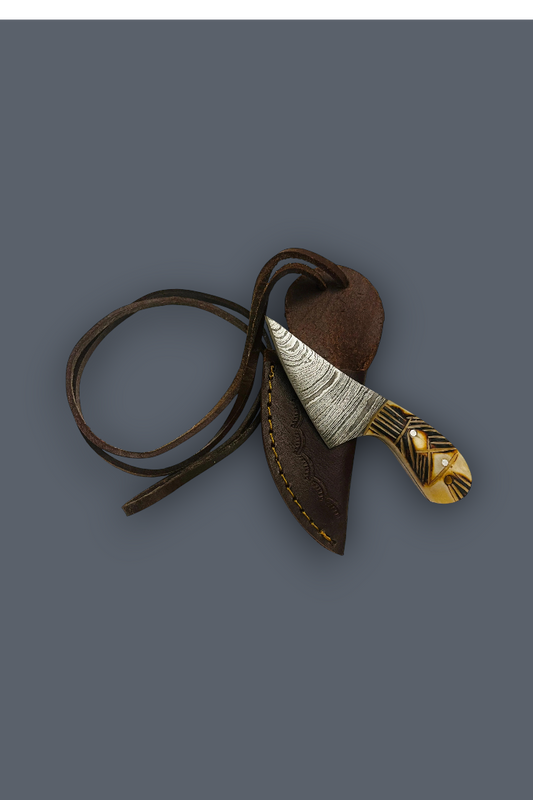 A decorative knife with a patterned silver and gold blade and handle, resting inside a brown leather sheath with a matching leather lanyard, set against a solid dark gray background.