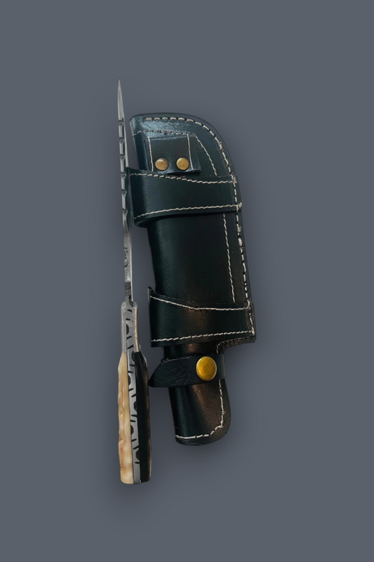 A fixed-blade knife with a patterned silver blade and a textured light handle, shown alongside its black leather sheath with white stitching and brass hardware, set against a solid dark gray background.