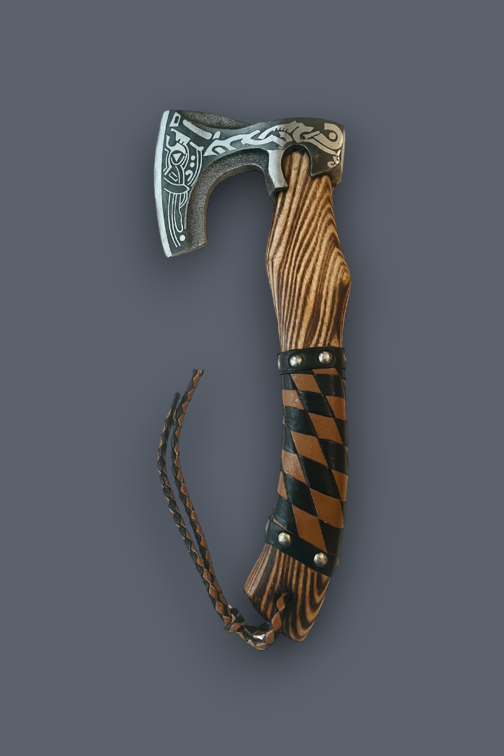A decorative Viking-style hand axe with an engraved silver steel head, a brown wood-grain handle, and a black-and-brown harlequin pattern wrapped around the middle, shown on a solid dark gray background.