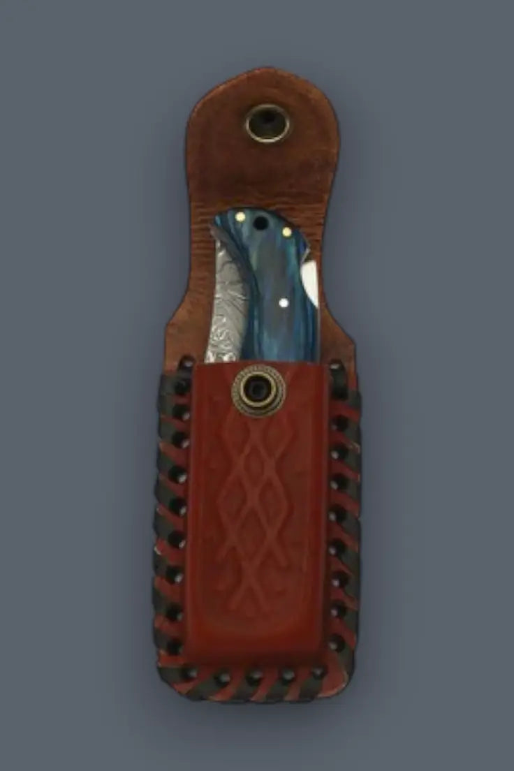 Blue handle Damascus folding knife securely stored inside a handcrafted leather EDC sheath.