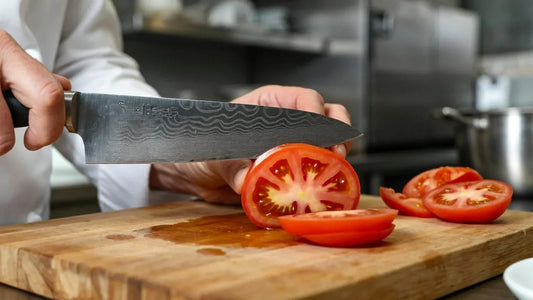 Chef slicing a tomato with a Damascus steel knife on a cutting board in the kitchen