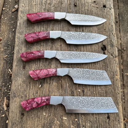 Five fixed-blade chef knives with patterned steel blades and red resin handles are arranged vertically on a rustic wooden plank.