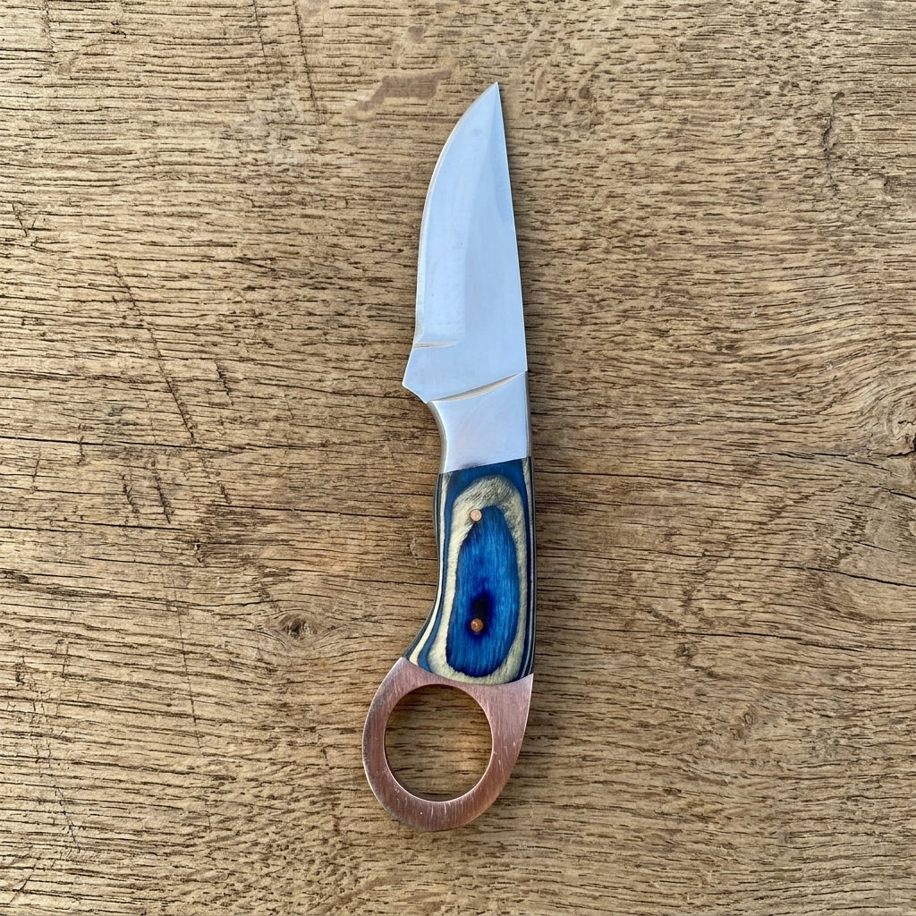 A small fixed-blade knife with a silver steel blade and a decorative handle made of layered blue, beige, and copper-colored wood, placed on a rustic wooden surface.