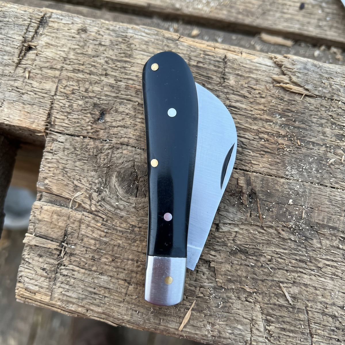 A folding pocket knife with a black handle and silver blade, resting on a rustic wooden plank.