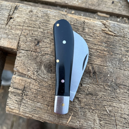 A folding pocket knife with a black handle and silver blade, resting on a rustic wooden plank.