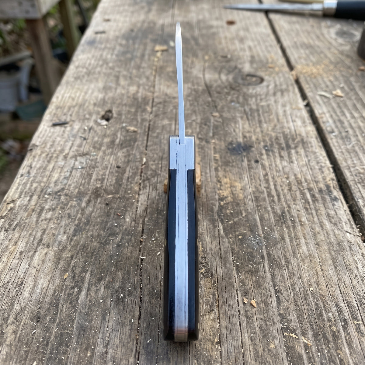 A folding pocket knife with a silver stainless steel blade and a dark brown wood handle, shown open on a rustic wooden plank surface.