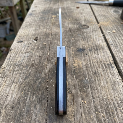 A folding pocket knife with a silver stainless steel blade and a dark brown wood handle, shown open on a rustic wooden plank surface.