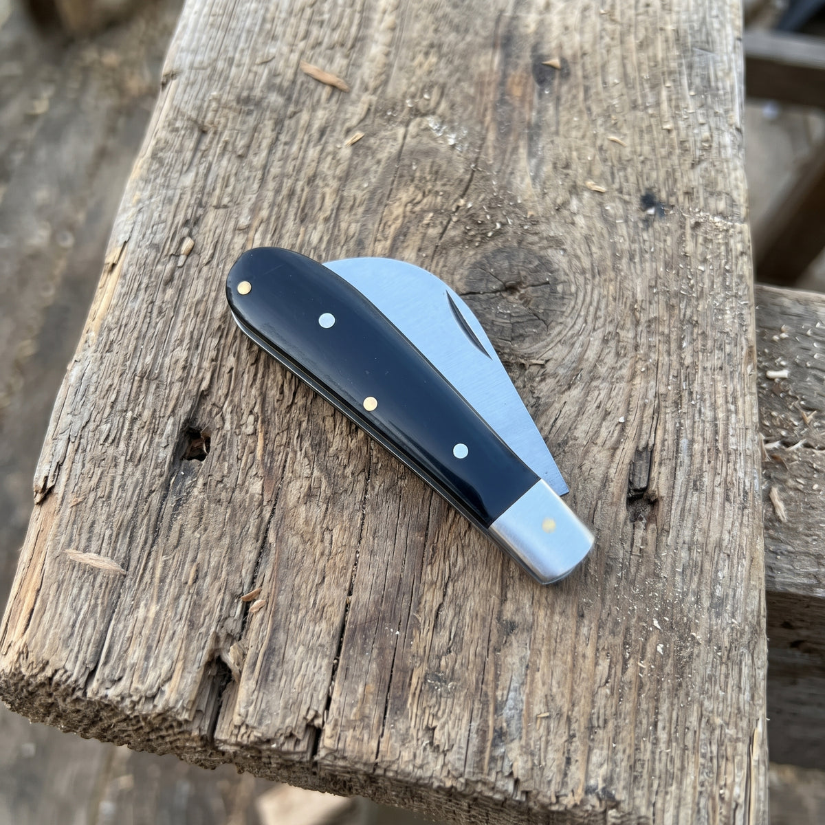 A classic folding pocket knife with a black handle and silver steel blade, resting on a rustic, weathered wooden plank.