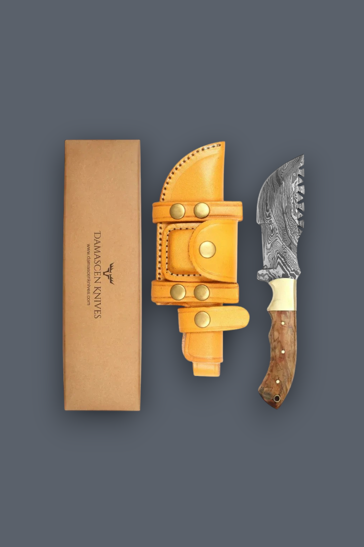 A fixed-blade knife with a patterned steel blade, a brown wood-grain handle, and a bright yellow leather sheath, displayed next to a tan cardboard box with the brand name 'TAMACON KNIVES' on a dark gray background.
