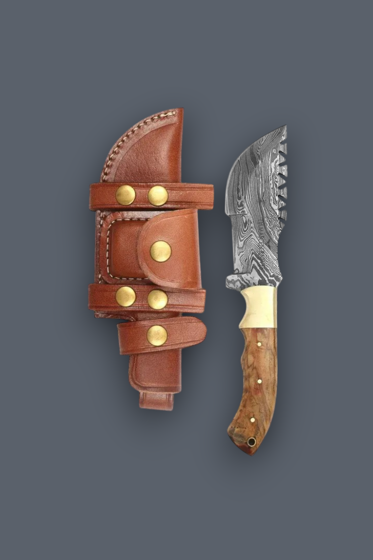 A fixed-blade knife with a patterned steel blade, a light wood handle, and a brass bolster, shown next to its brown leather sheath with brass rivets on a dark gray background.