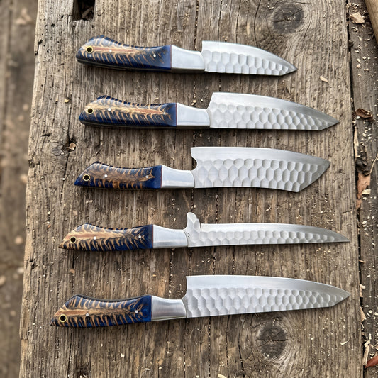 Five fixed-blade knives with hammered steel blades and patterned blue-and-gold handles, arranged vertically on a rustic wooden surface.