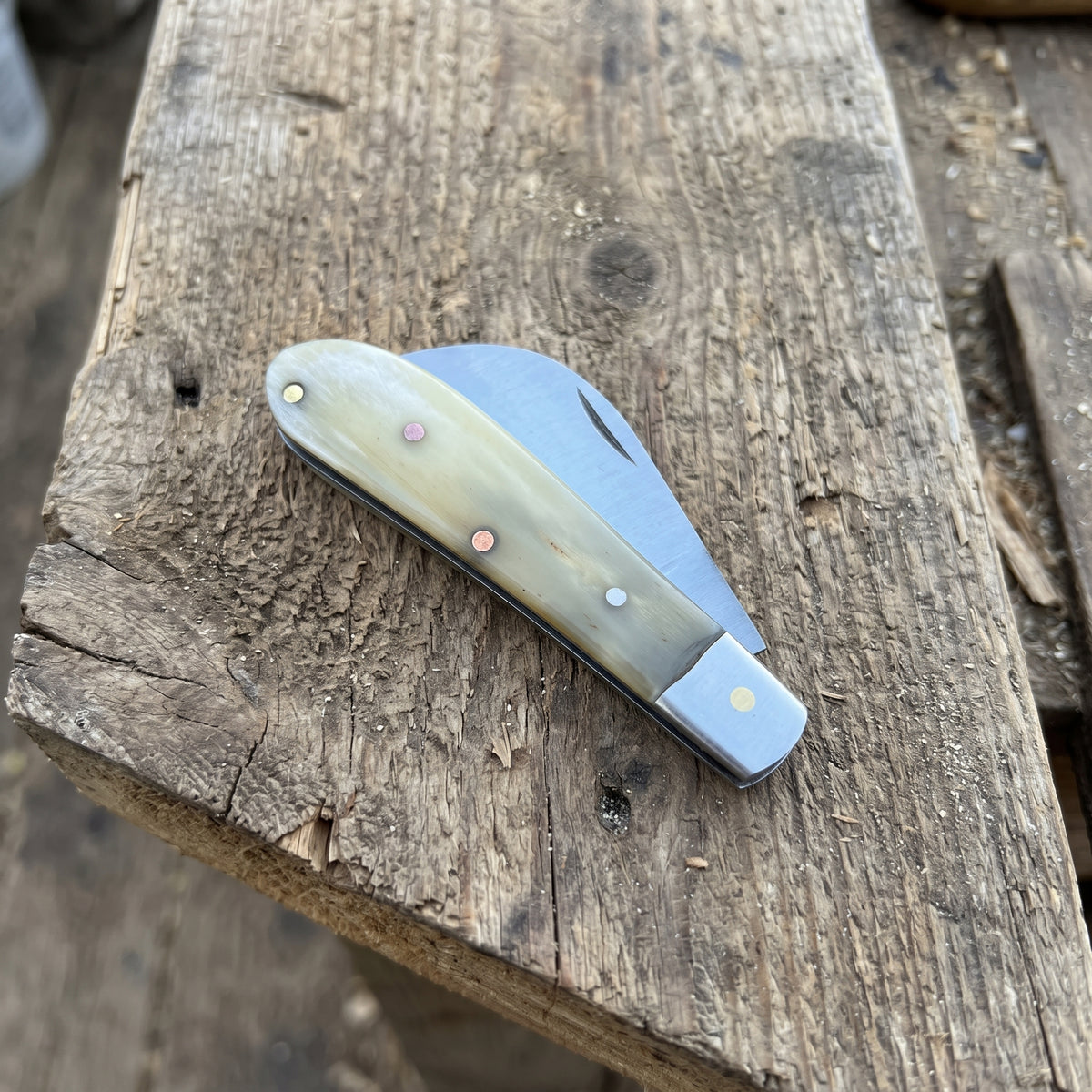 A classic folding pocket knife with a cream and brown bone handle and a silver steel blade, resting on a rustic wooden plank.