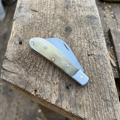 A classic folding pocket knife with a cream and brown bone handle and a silver steel blade, resting on a rustic wooden plank.