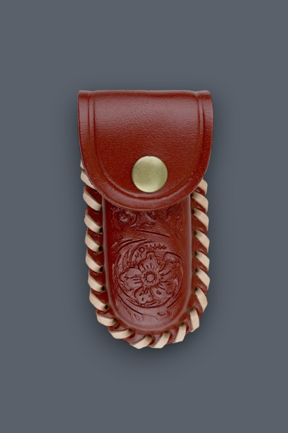 A reddish-brown leather pouch with a snap closure, featuring an embossed floral design and twisted cream-colored trim, shown against a solid dark gray background.