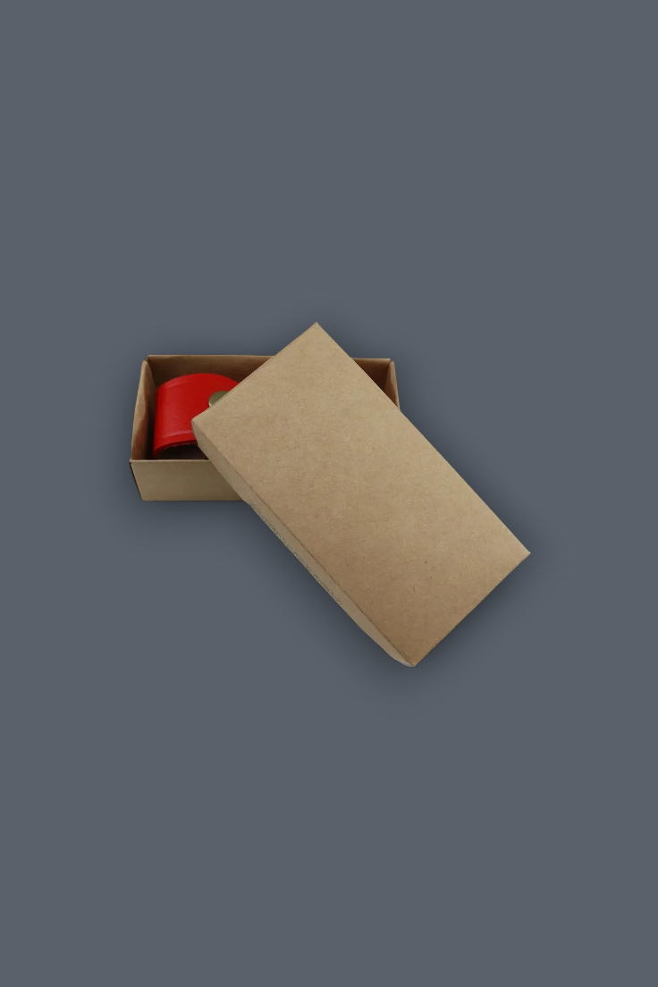 A brown kraft paper box with its lid leaning against the front, containing a bright red cylindrical item, set against a solid dark gray background.