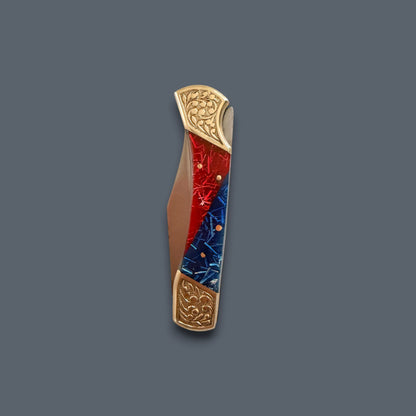 A folding pocket knife with a red and blue marbled inlay on the blade, accented with gold-toned metal end caps and a brown leather-wrapped handle, shown on a solid dark gray background.