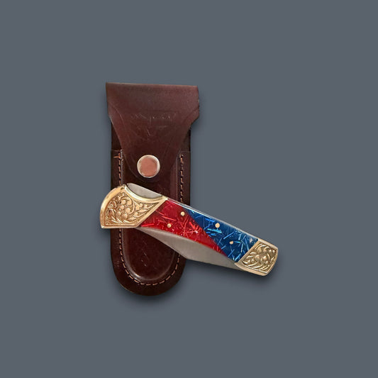 A folding pocket knife with a red and blue inlay handle and gold-toned metal accents, shown partially inserted into a brown leather sheath against a dark gray background.