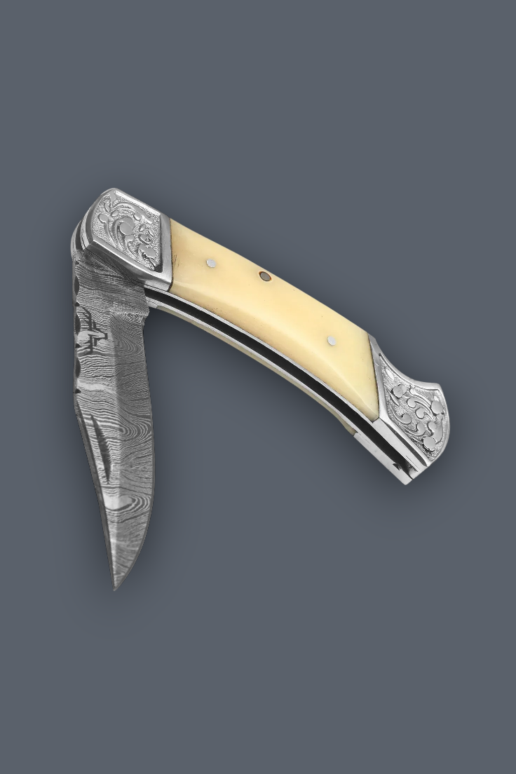 A folding pocket knife with a Damascus steel blade, ornate silver-toned metal end caps, and a cream-colored handle inlay, shown against a solid dark gray background.