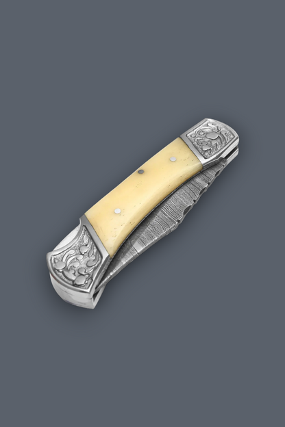 A folding pocket knife with a pale yellow bone or horn handle, silver-toned engraved metal end pieces, and a partially serrated steel blade, shown on a solid dark gray background.