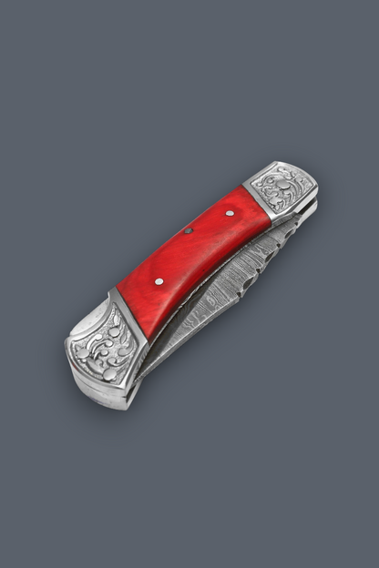 A folding pocket knife with a bright red handle scale and ornate silver-toned metal guard and bolster, shown open on a solid dark gray background.
