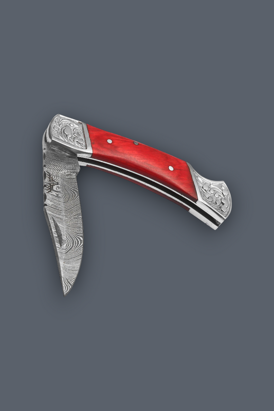 A folding pocket knife with a Damascus steel blade, red handle scales, and silver-toned engraved metal accents, shown on a solid dark gray background.