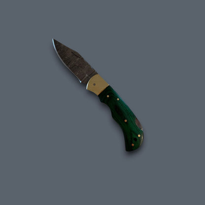 A pocket knife with a dark patterned steel blade, a brass bolster, and a dark green wood handle with brass pins, shown on a solid dark gray background.