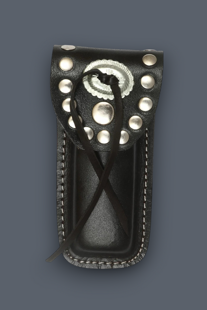 A black leather knife sheath with silver conchos and studs, featuring a braided black leather lanyard, shown against a solid dark gray background.