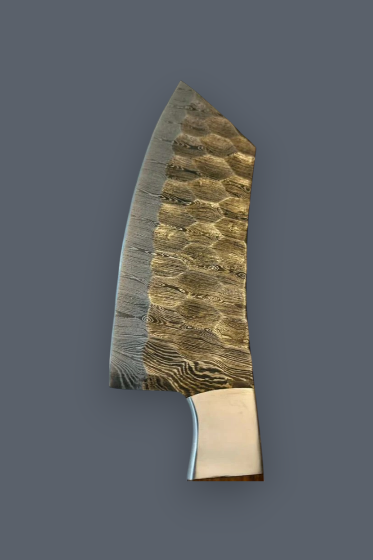 A custom handmade kitchen knife with a textured, hammered steel blade and a polished brass bolster, shown against a solid dark gray background.