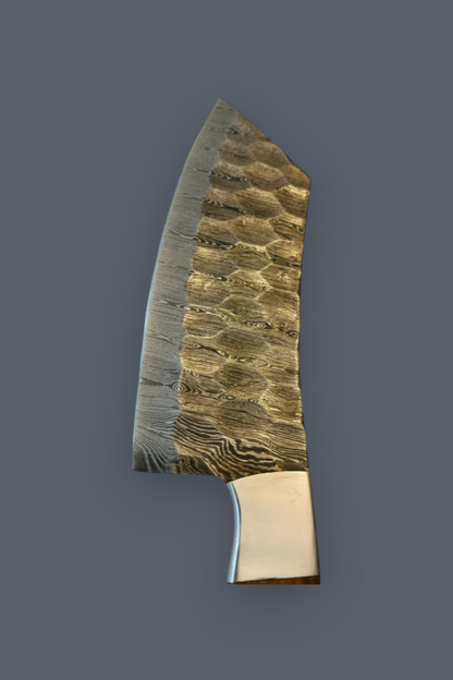 A custom handmade kitchen knife with a textured, hammered steel blade and a polished brass bolster, shown against a solid dark gray background.