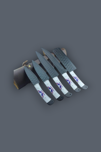 A set of five knives with textured gray blades and white handles featuring purple and blue graphic designs, displayed next to a dark leather sheath on a solid dark gray background.