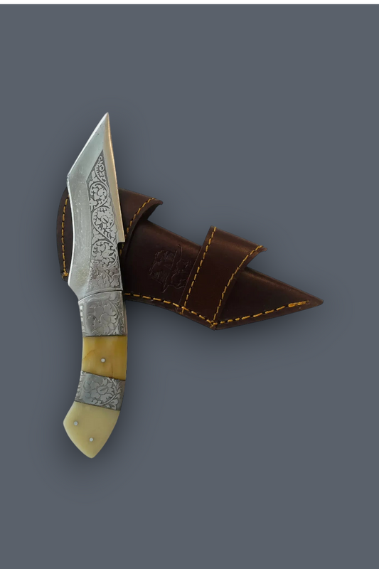 A decorative fixed-blade knife with a patterned steel blade, silver-toned metal bolster, and cream-colored handle scales, shown next to its brown leather sheath on a solid dark gray background.