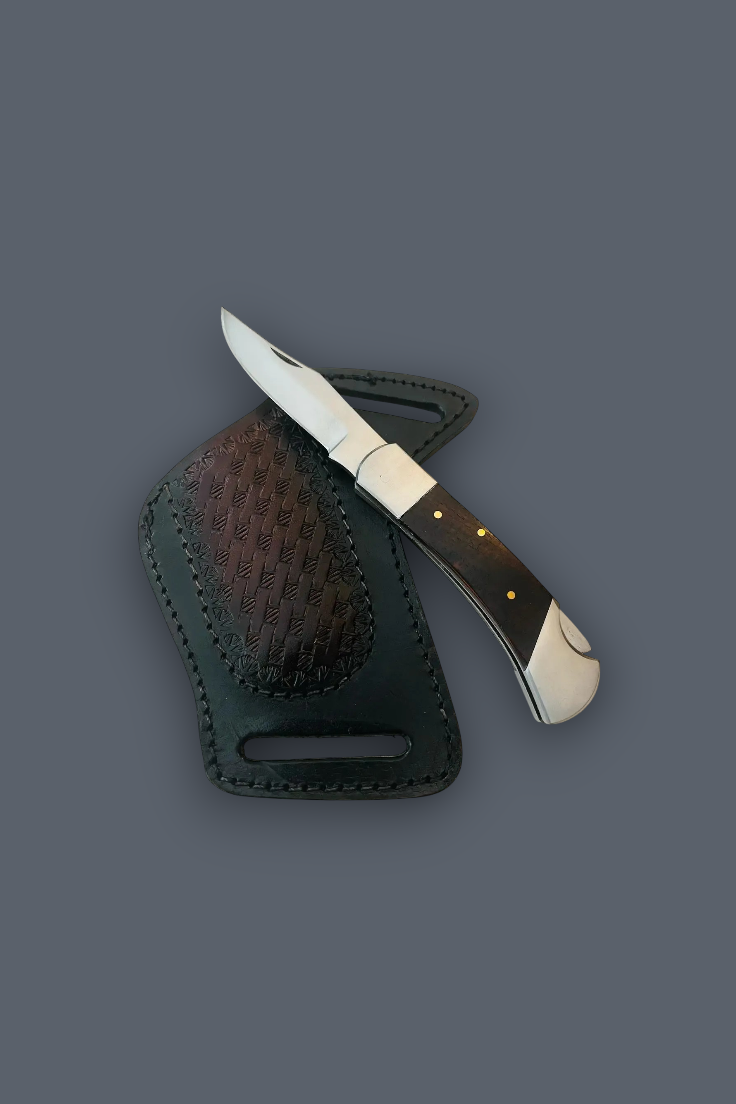 A folding pocket knife with a dark wood handle and white end pieces rests diagonally across a dark brown leather sheath on a solid dark gray background.