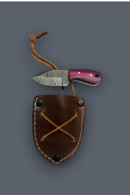 A fixed-blade knife with a patterned steel blade and a pinkish-purple handle, shown resting on top of a brown leather sheath with a tan cord loop, against a solid dark gray background.