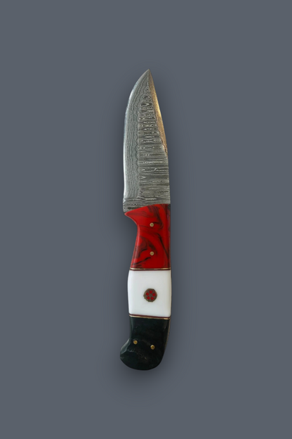 A small fixed-blade knife with a patterned steel blade, a red and white handle, and a black end, shown vertically against a solid dark gray background.