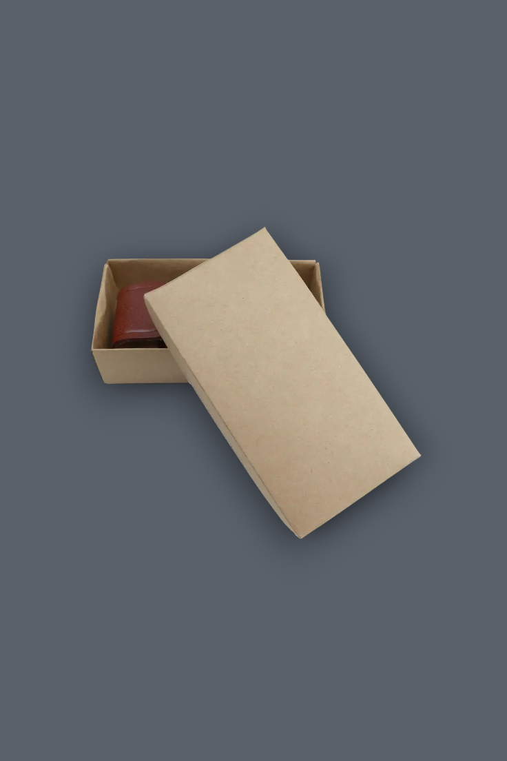 A kraft paper gift box with its lid leaning against the front, showing a small reddish-brown item inside on a dark gray background.