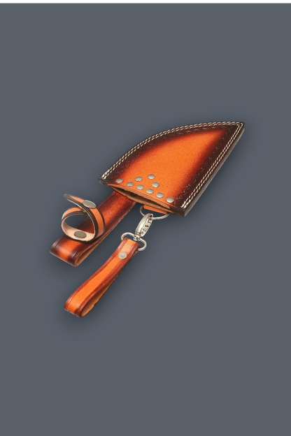 A brown leather knife sheath with a matching wrist strap and metal snap clasp, shown on a solid dark gray background.
