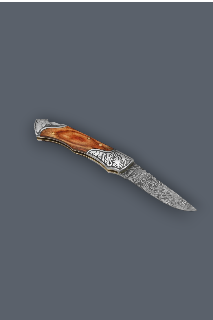 A folding pocket knife with a patterned Damascus steel blade, engraved silver-toned metal end caps, and a curved amber-brown handle inlay, shown on a solid dark gray background.