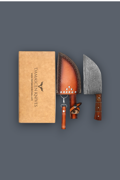 Damascus Knives product display featuring a tan leather sheath, a steel knife with a dark wood handle, and a matching leather sheath with a wooden handle, arranged next to a tan branded presentation box on a dark gray background.