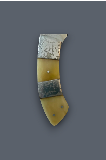 A vintage-style curved knife or tool handle made of pale yellow bone or horn with two silver-toned metal bands featuring engraved floral or leaf patterns, shown on a solid dark gray background.