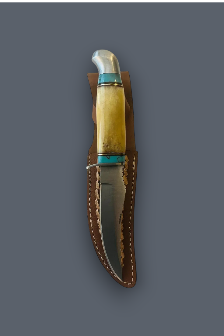 A fixed-blade knife with a polished steel blade, a cream-colored bone handle, and turquoise-colored inlay, shown resting inside a brown leather sheath against a solid dark gray background.