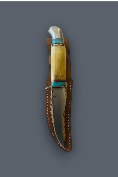 A fixed-blade knife with a polished steel blade, a cream-colored bone handle, and turquoise-colored inlay, shown resting inside a brown leather sheath against a solid dark gray background.