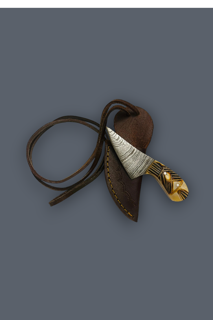 A decorative knife with a patterned silver and gold blade and handle, resting inside a brown leather sheath with a matching leather lanyard, set against a solid dark gray background.