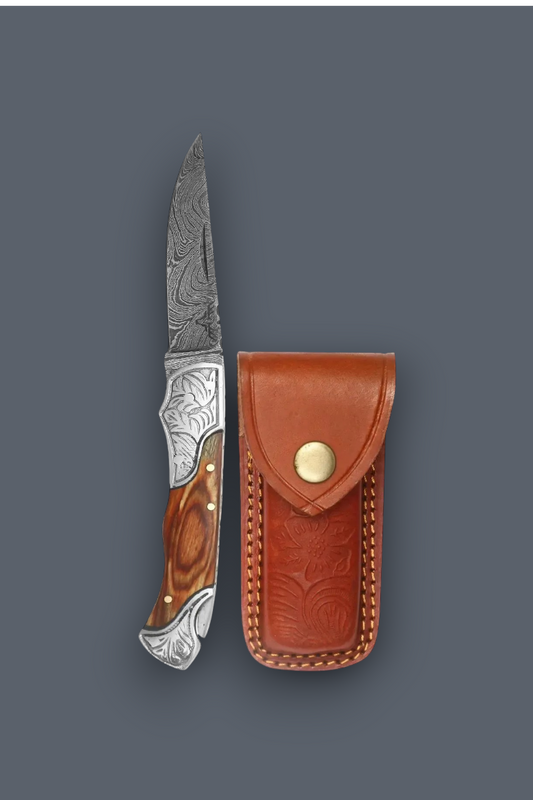 A folding pocket knife with a patterned steel blade, engraved silver handle, and brown wood handle, shown next to its brown leather sheath on a dark gray background.