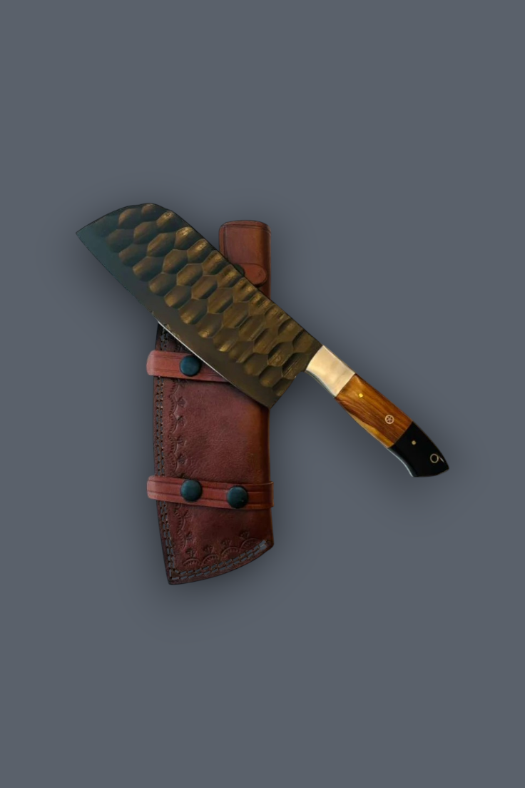 A large knife with a hammered dark metal blade and a brown wooden handle, shown resting on top of a brown leather sheath against a solid dark gray background.