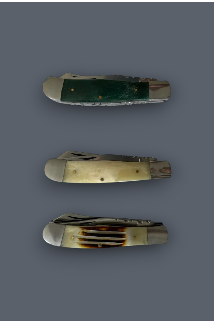 Three folding pocket knives with different handle materials are arranged vertically on a solid dark gray background. The top knife has a dark green handle, the middle has a cream bone handle, and the bottom has a horn handle with dark brown mottling.