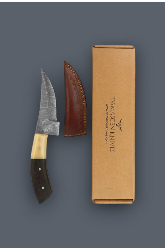 Damascen Knives knife with a patterned steel blade, dark wood handle, and brown leather sheath, displayed next to its kraft paper packaging box on a dark gray background.