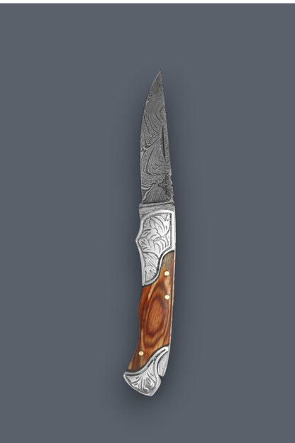 A folding pocket knife with a patterned Damascus steel blade, an engraved silver metal bolster, and a brown wood handle, shown against a solid dark gray background.