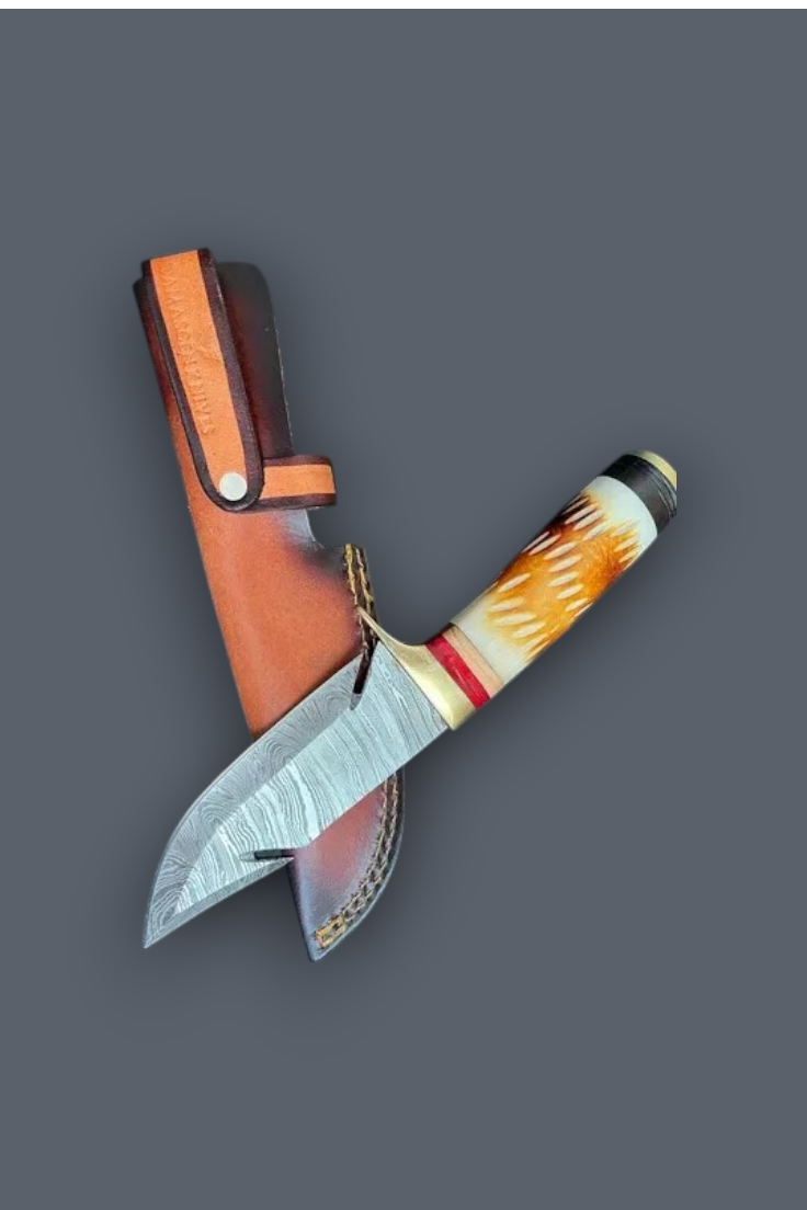 A custom fixed-blade knife with a patterned orange and white handle, a textured steel blade, and a brown leather sheath, arranged diagonally on a solid dark gray background.