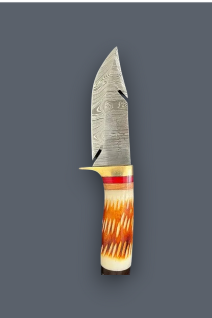 A fixed-blade knife with a patterned Damascus steel blade, a brass guard, and a carved handle made from natural horn with orange, brown, and cream tones, shown against a solid dark gray background.